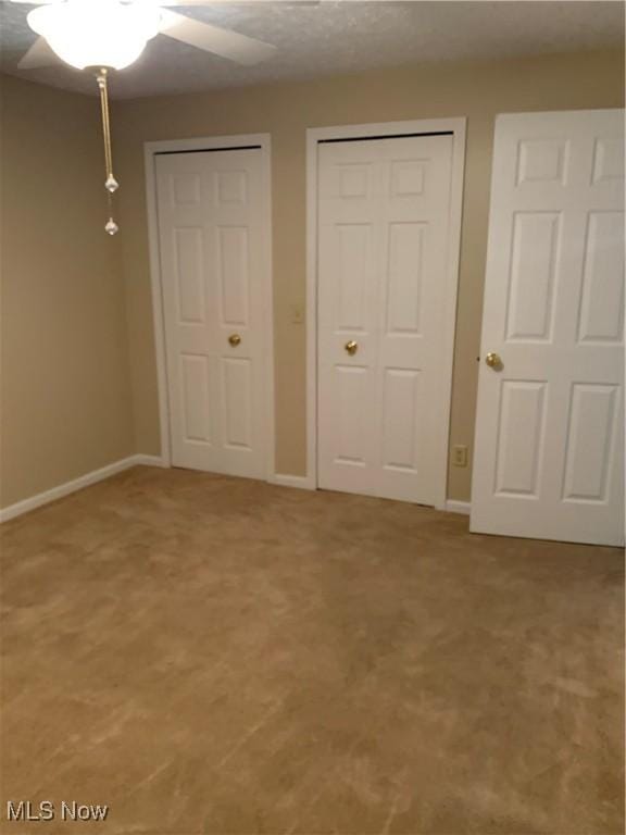 unfurnished bedroom featuring carpet flooring, multiple closets, and ceiling fan