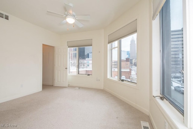empty room with light carpet, visible vents, baseboards, and ceiling fan