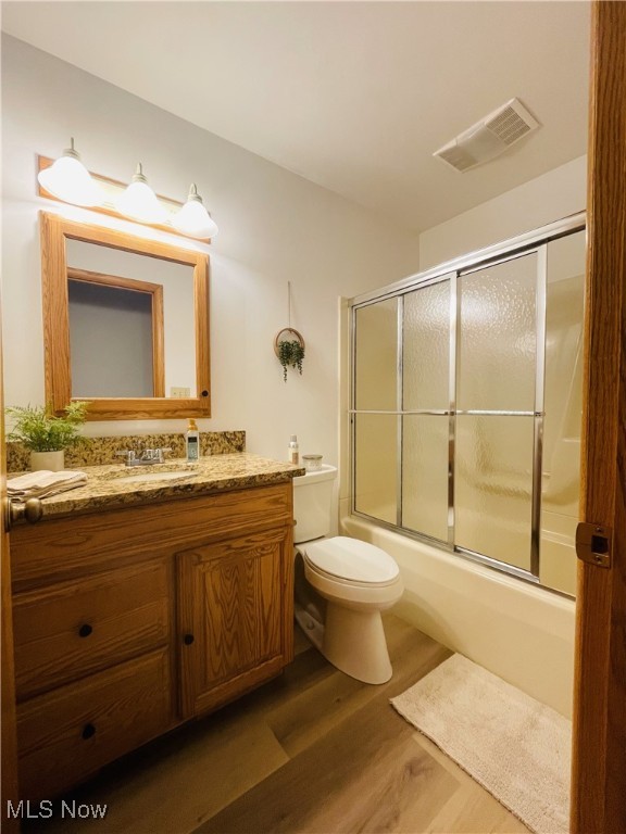 full bathroom featuring hardwood / wood-style floors, vanity, toilet, and bath / shower combo with glass door