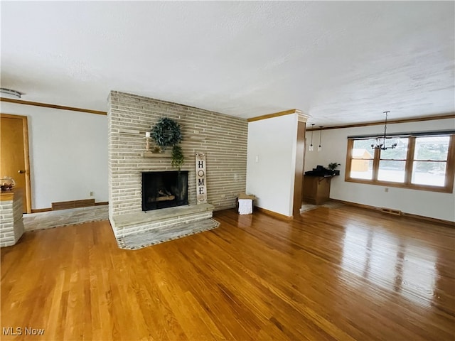 unfurnished living room featuring hardwood / wood-style floors, a notable chandelier, crown molding, and a fireplace