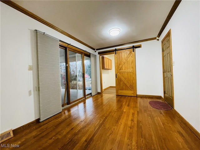 empty room with a barn door, wood-type flooring, and ornamental molding