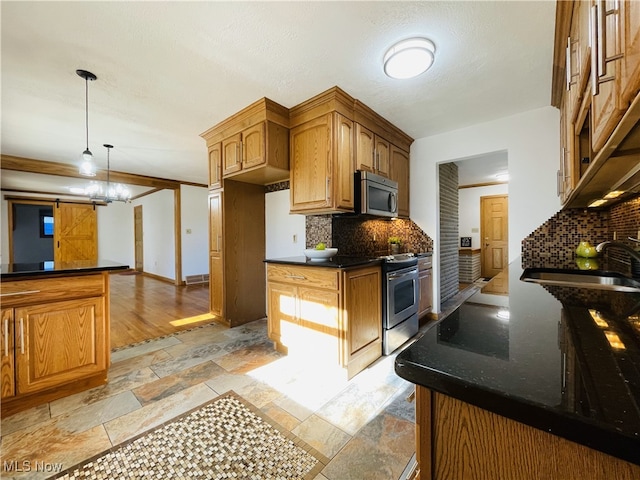 kitchen with pendant lighting, sink, decorative backsplash, a barn door, and appliances with stainless steel finishes