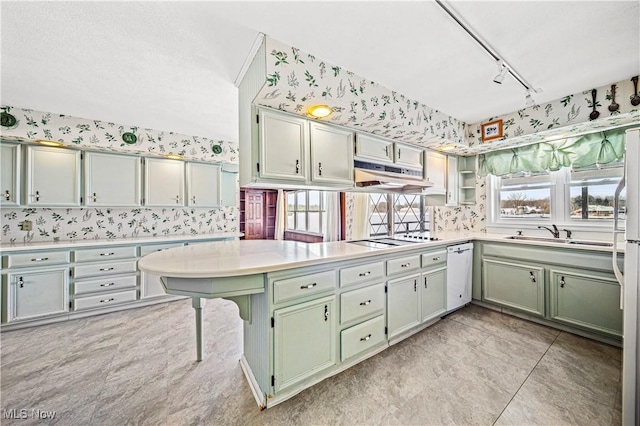 kitchen featuring white appliances, under cabinet range hood, a sink, green cabinetry, and rail lighting