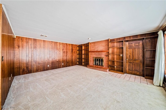 unfurnished living room featuring wooden walls, carpet floors, built in features, and a brick fireplace