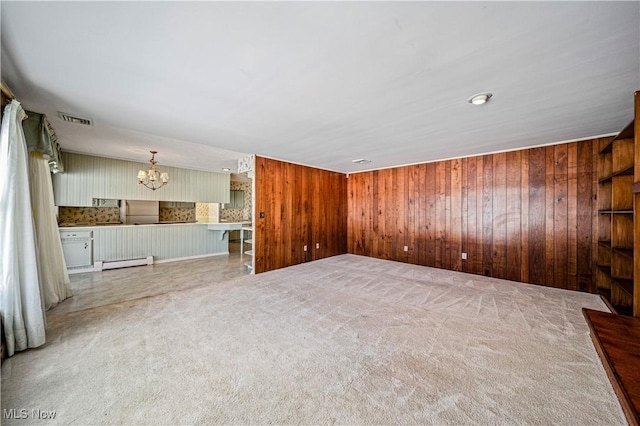 unfurnished living room with baseboard heating, a chandelier, wooden walls, and carpet flooring