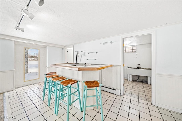 kitchen featuring a textured ceiling, rail lighting, light tile patterned floors, a center island with sink, and a breakfast bar area