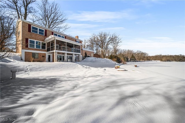 snow covered back of property with a sunroom