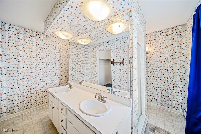 bathroom featuring wallpapered walls, baseboards, double vanity, and a shower stall