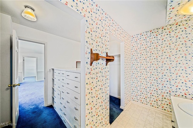 bathroom featuring baseboards, wallpapered walls, and vanity