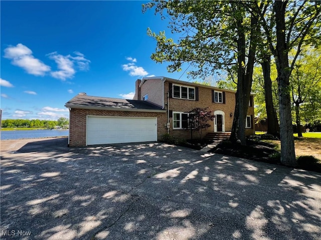 view of front of house with a garage, concrete driveway, brick siding, and a water view