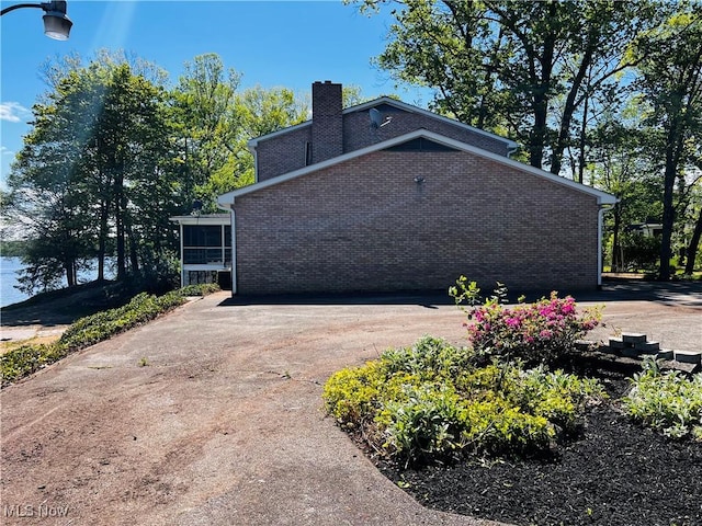 view of side of property with a chimney, a sunroom, and brick siding