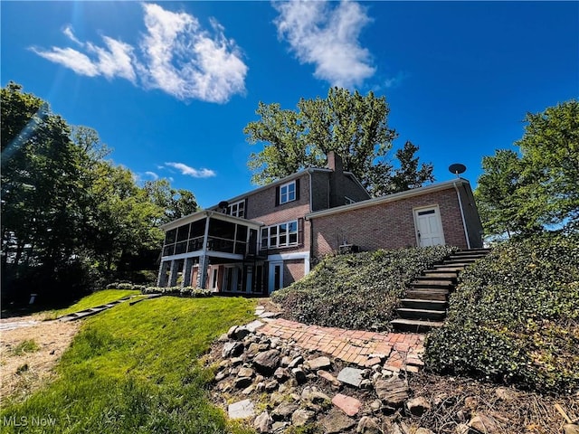 back of property featuring a sunroom, stairs, a lawn, brick siding, and a chimney