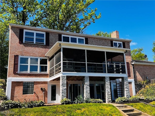 view of front facade featuring a sunroom, a chimney, brick siding, and stone siding