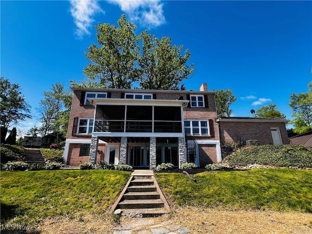 back of house with a chimney, brick siding, and a sunroom