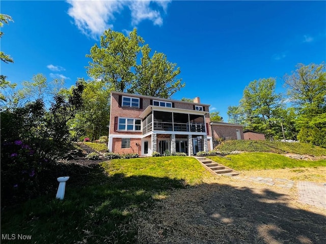 rear view of property with a sunroom, a chimney, brick siding, and a lawn