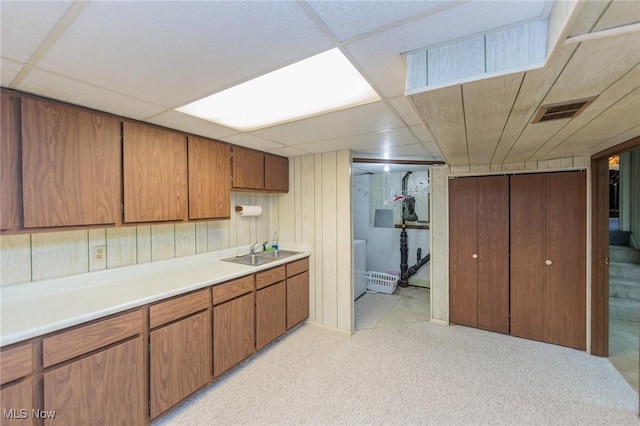 kitchen featuring sink, wood walls, light colored carpet, washer / dryer, and a paneled ceiling