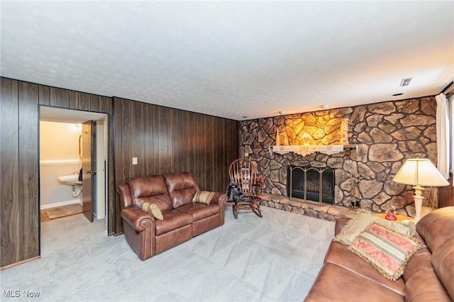 carpeted living room with wood walls, a fireplace, and a textured ceiling