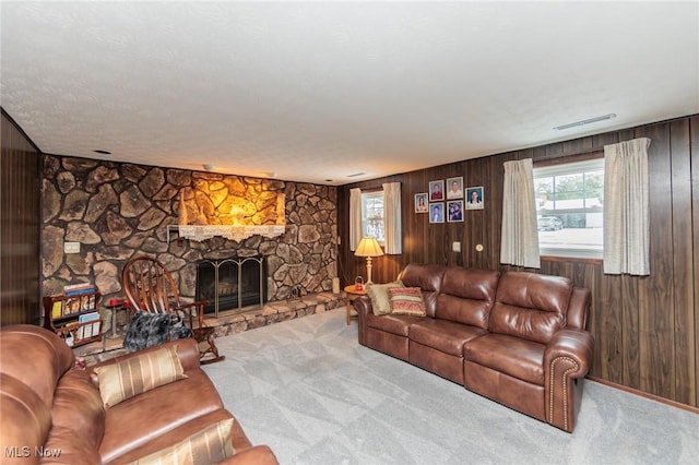 carpeted living room featuring a stone fireplace, a textured ceiling, and wooden walls