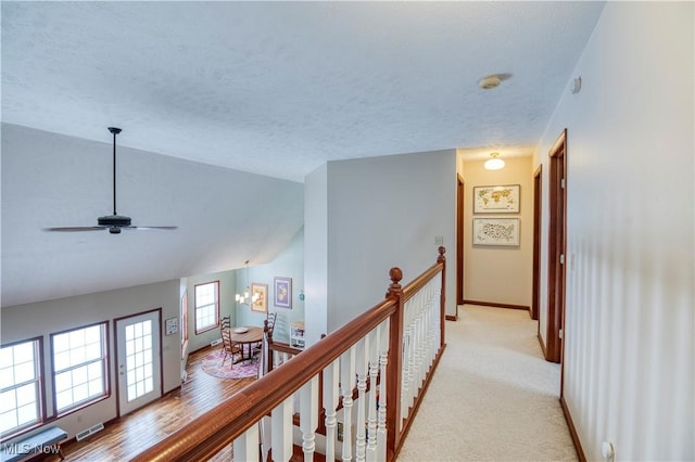 hallway with a textured ceiling, a chandelier, light carpet, and vaulted ceiling