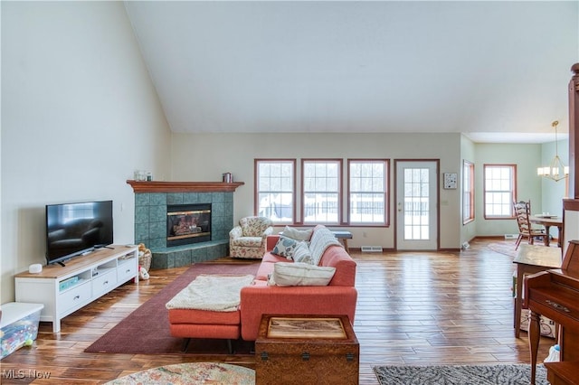 living room with vaulted ceiling, an inviting chandelier, wood-type flooring, and a tiled fireplace