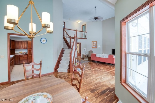 dining room with a towering ceiling, ceiling fan with notable chandelier, and light hardwood / wood-style flooring