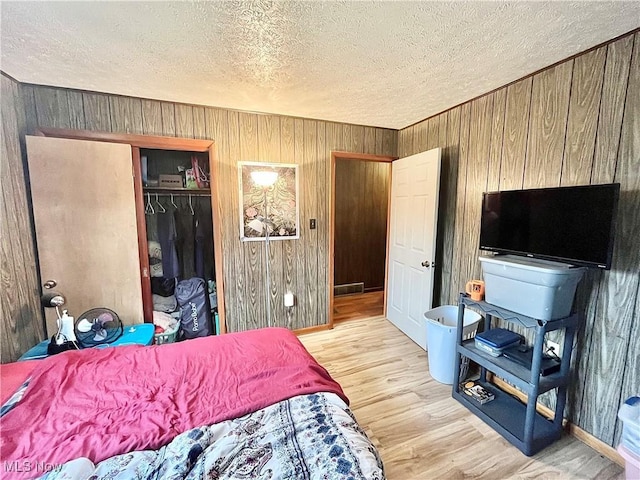 bedroom featuring wood walls, a closet, light hardwood / wood-style floors, and a textured ceiling