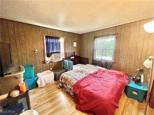 bedroom featuring wooden walls, cooling unit, a textured ceiling, and hardwood / wood-style flooring