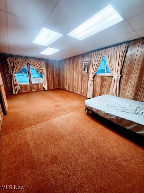 unfurnished bedroom with light carpet, a drop ceiling, and wooden walls