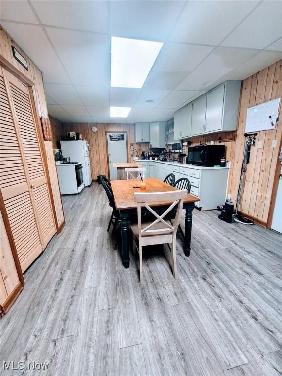 dining space featuring light hardwood / wood-style floors, a drop ceiling, and wooden walls