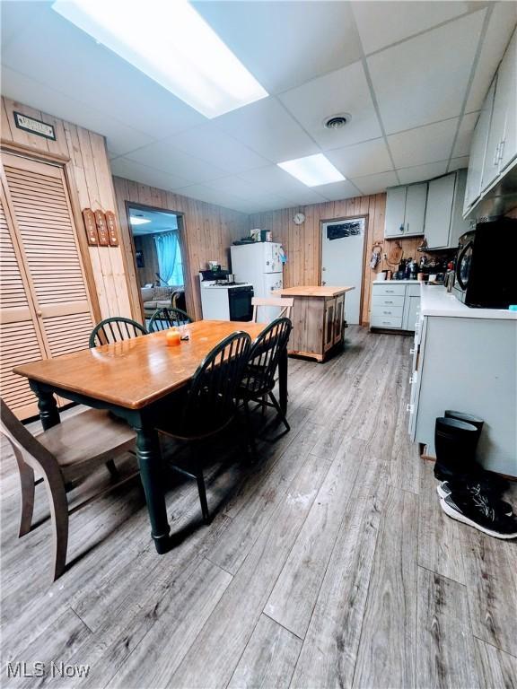 dining space with light wood-type flooring, a paneled ceiling, and wooden walls