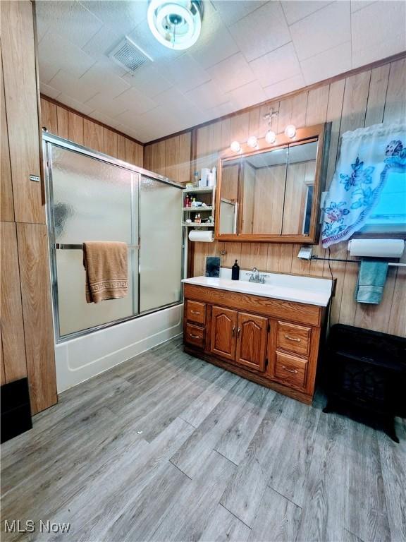 bathroom with wood walls, vanity, enclosed tub / shower combo, and wood-type flooring