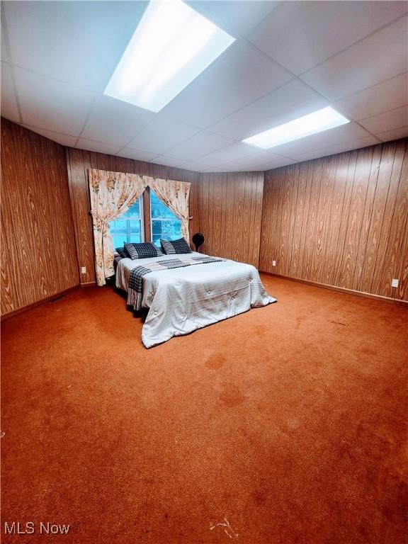 unfurnished bedroom featuring carpet flooring, a paneled ceiling, and wood walls