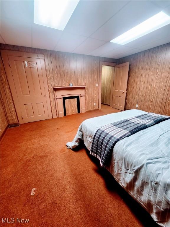 carpeted bedroom featuring a paneled ceiling and wooden walls