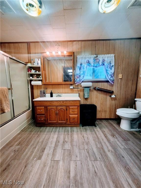 full bathroom featuring vanity, wood-type flooring, enclosed tub / shower combo, toilet, and wood walls