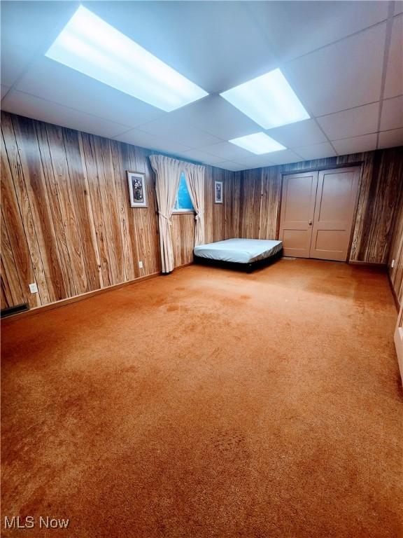 unfurnished bedroom featuring light carpet, a paneled ceiling, and wooden walls