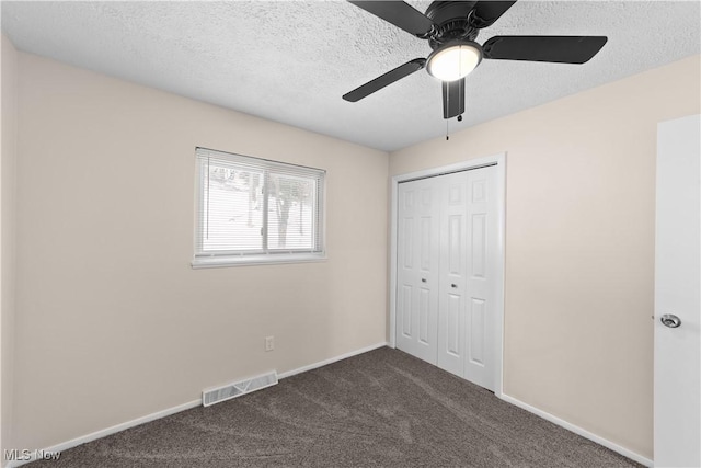 unfurnished bedroom featuring dark colored carpet, a textured ceiling, a closet, and ceiling fan