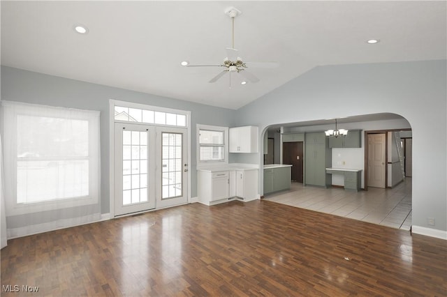 unfurnished living room featuring high vaulted ceiling, a healthy amount of sunlight, ceiling fan with notable chandelier, and hardwood / wood-style flooring