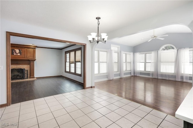 unfurnished living room with a large fireplace, ceiling fan with notable chandelier, a healthy amount of sunlight, and light tile patterned floors