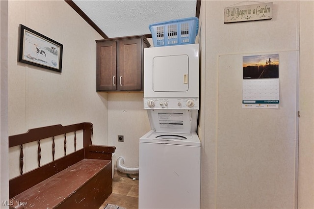 laundry area featuring a textured ceiling, cabinets, stacked washer / drying machine, and ornamental molding