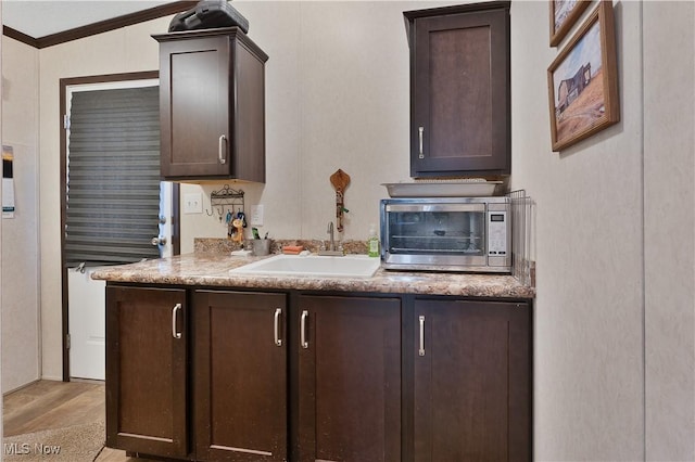 kitchen with dark brown cabinetry, ornamental molding, and sink