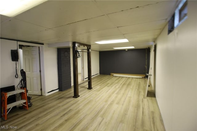 basement with light wood-type flooring and a paneled ceiling