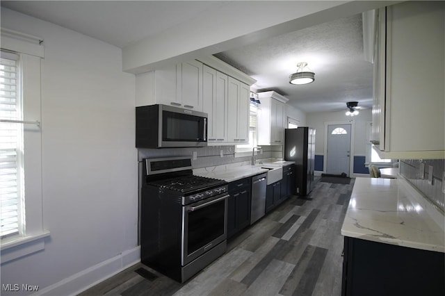 kitchen with light stone counters, dark hardwood / wood-style flooring, decorative backsplash, white cabinets, and appliances with stainless steel finishes