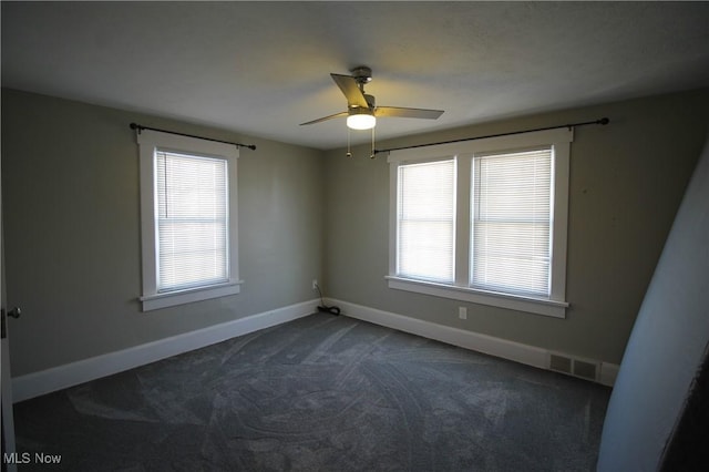 unfurnished room with dark colored carpet, ceiling fan, and a healthy amount of sunlight