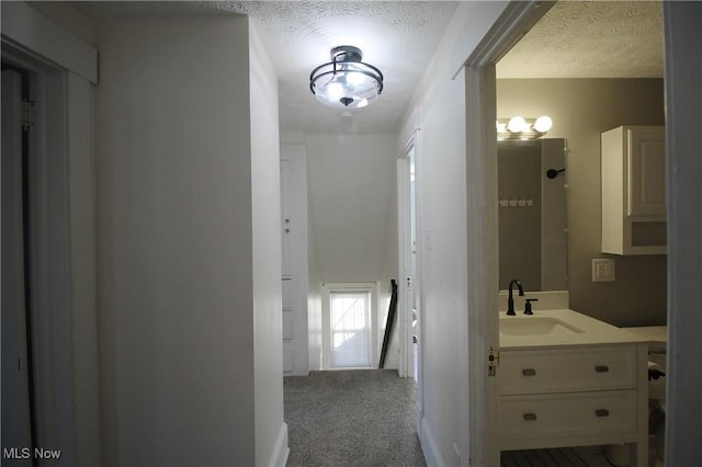 hallway with a textured ceiling, sink, and light carpet