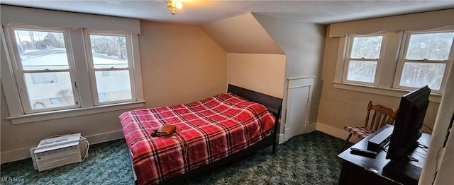 bedroom with dark colored carpet, vaulted ceiling, and multiple windows