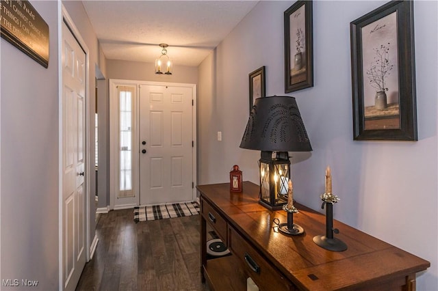 foyer entrance with a textured ceiling, dark wood-type flooring, and a chandelier