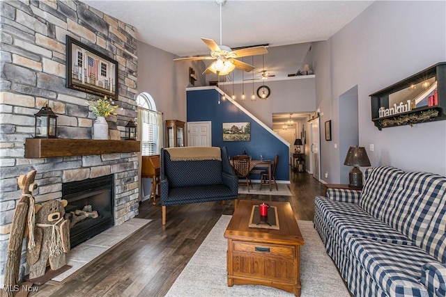 living room with dark hardwood / wood-style floors, ceiling fan, a stone fireplace, and high vaulted ceiling