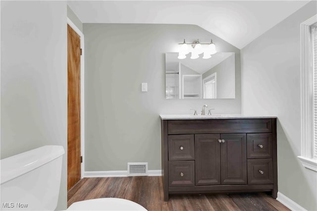 bathroom featuring hardwood / wood-style flooring, vanity, toilet, and lofted ceiling