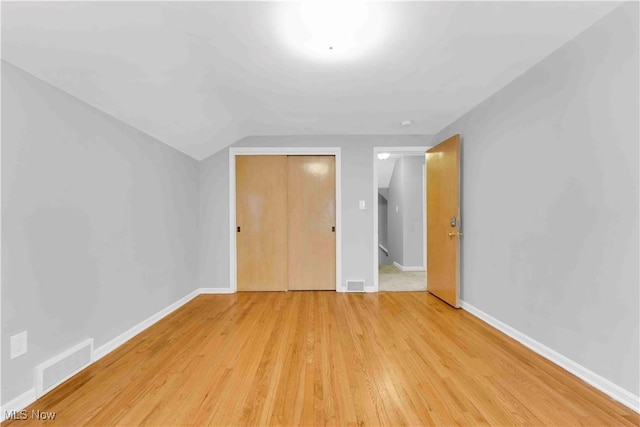 unfurnished bedroom featuring light hardwood / wood-style floors, vaulted ceiling, and a closet