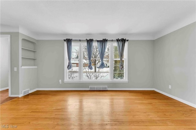 spare room with built in shelves and light hardwood / wood-style flooring